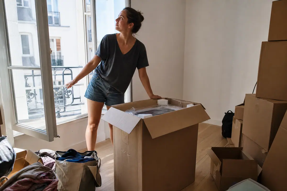 Une jeune locataire vérifie l'encadrement de sa fenêtre avant d'installer un climatiseur mobile le jour de son emménagement