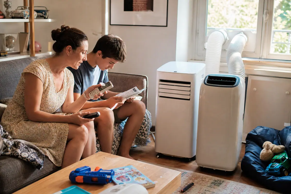 Une mère et son fils comparent les télécommandes de deux climatiseurs mobiles installés côte à côte dans leur salon