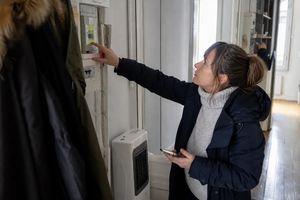 Une femme vérifie sa consommation électrique près d'un radiateur d'appoint dans son couloir