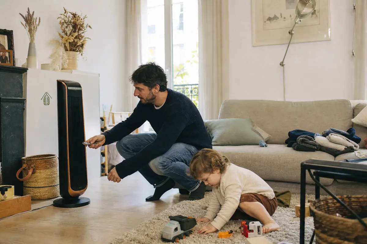 Un père règle un radiateur d'appoint moderne à la télécommande alors que son enfant joue à proximité