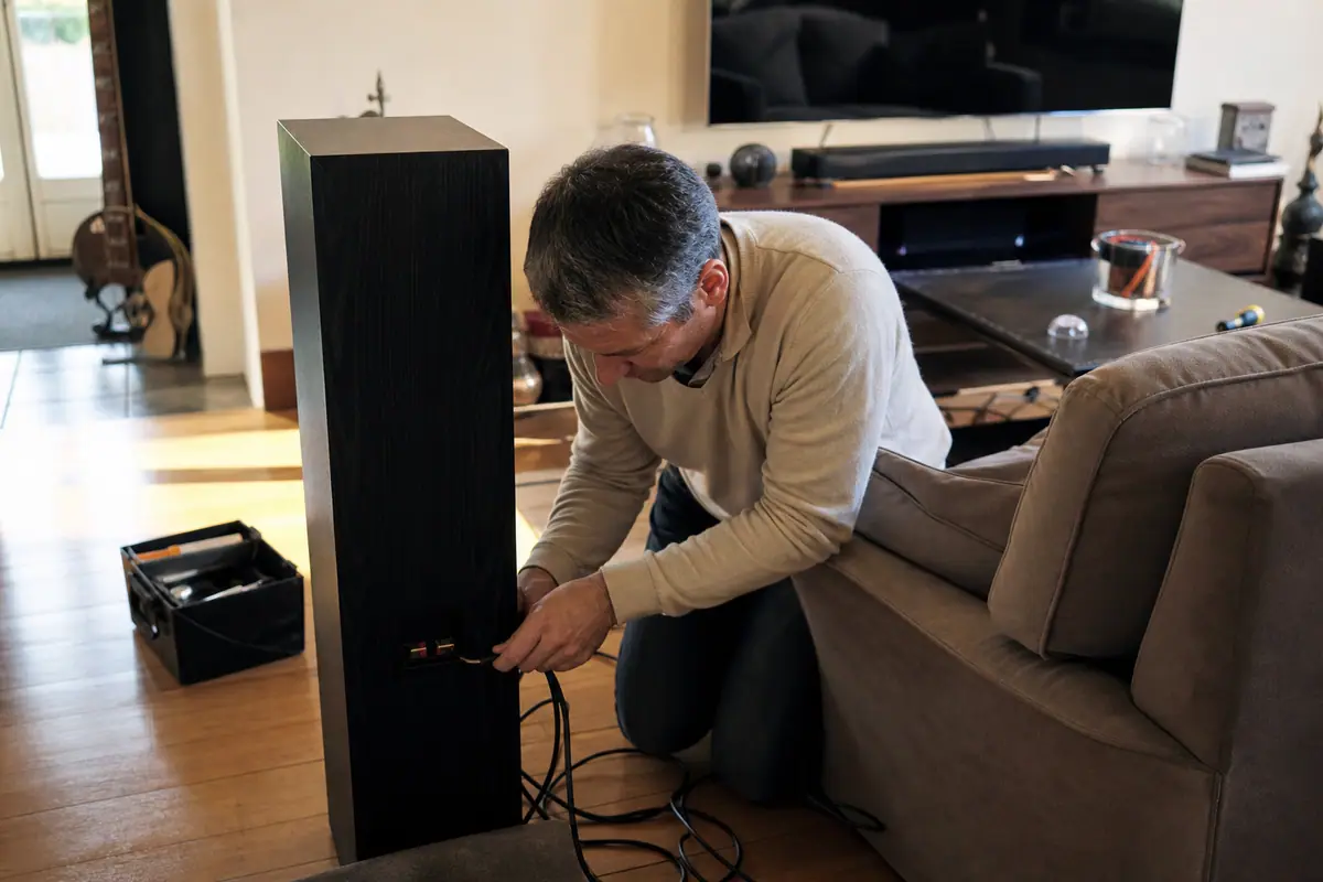 Un homme installe des enceintes de home cinéma dans son salon, avec une barre de son visible sous le téléviseur