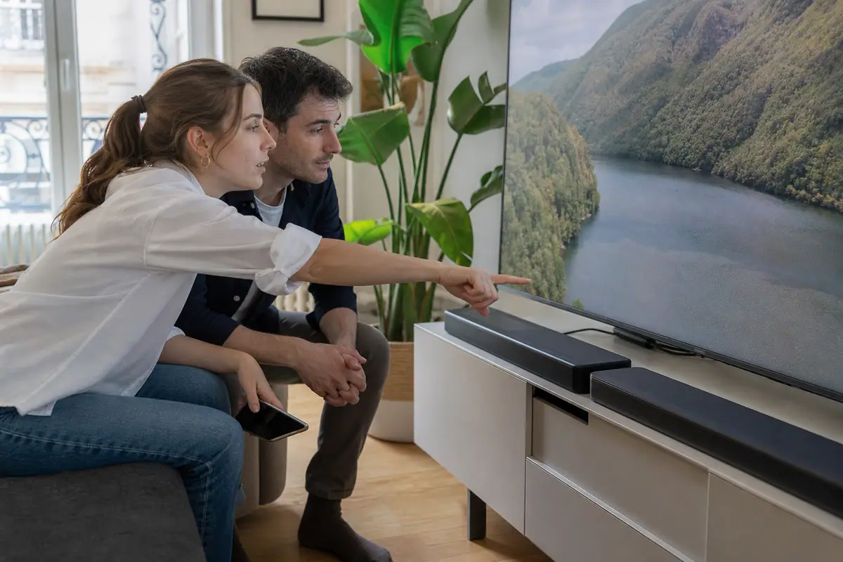 Un couple compare deux barres de son posées sous leur téléviseur avant d'acheter