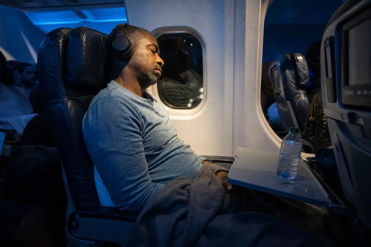 Un homme dort paisiblement avec un casque à réduction de bruit sur les oreilles pendant un vol de nuit