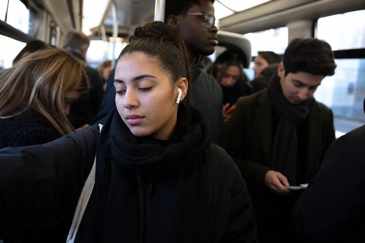 Une jeune femme détendue écoute de la musique avec des écouteurs sans fil dans un métro bondé