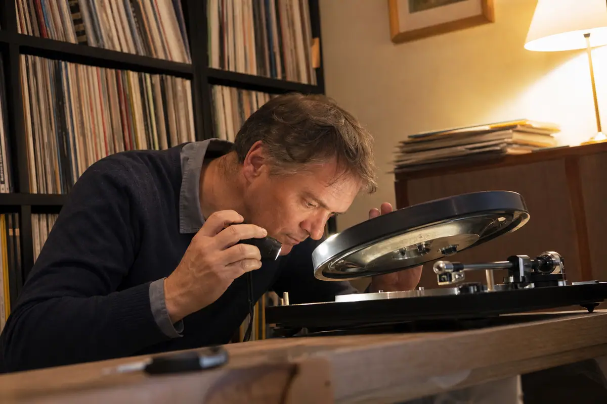 Un homme examine le mécanisme d'entraînement sous le plateau d'une platine vinyle