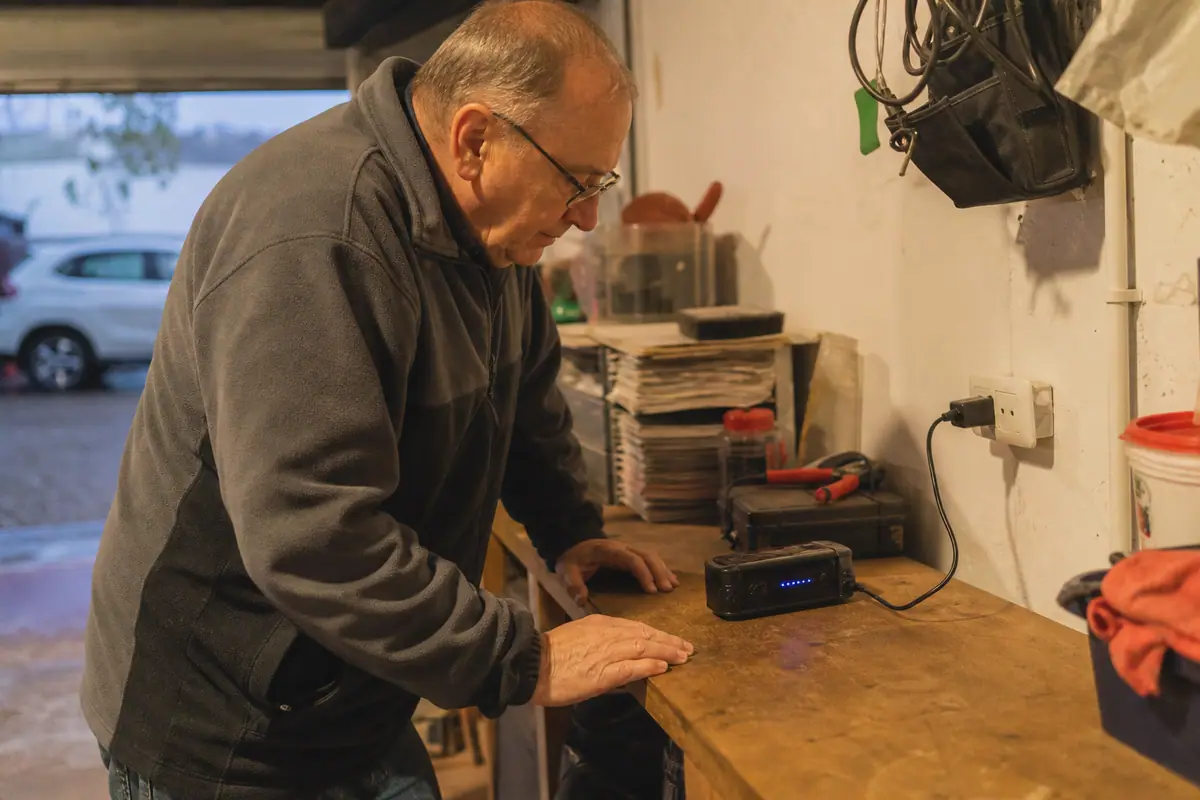 Un homme vérifie le niveau de charge d'un booster de batterie branché sur une prise dans son garage