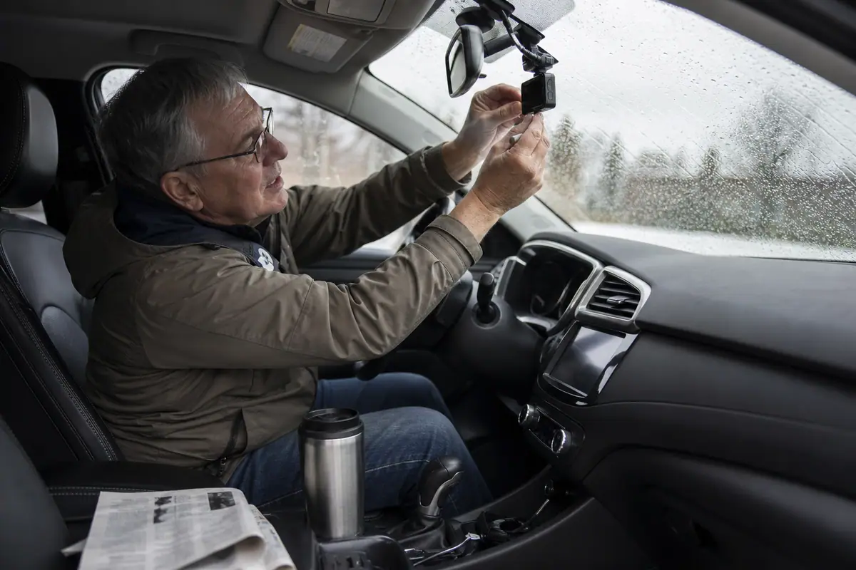 Un homme âgé insère une carte mémoire dans la dashcam fixée au pare-brise de sa voiture un jour de pluie