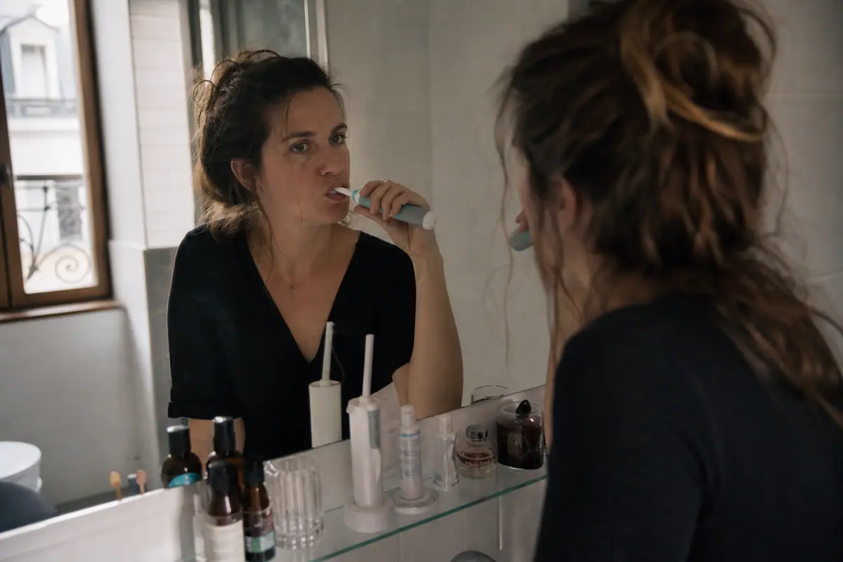Une femme se brosse les dents avec une brosse à dents électrique devant le miroir de sa salle de bain