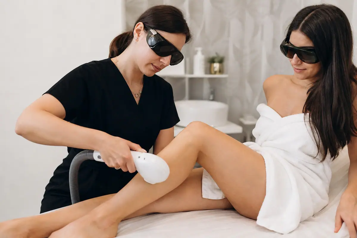Une esthéticienne réalise une séance de lumière pulsée professionnelle sur la jambe d'une cliente dans un institut