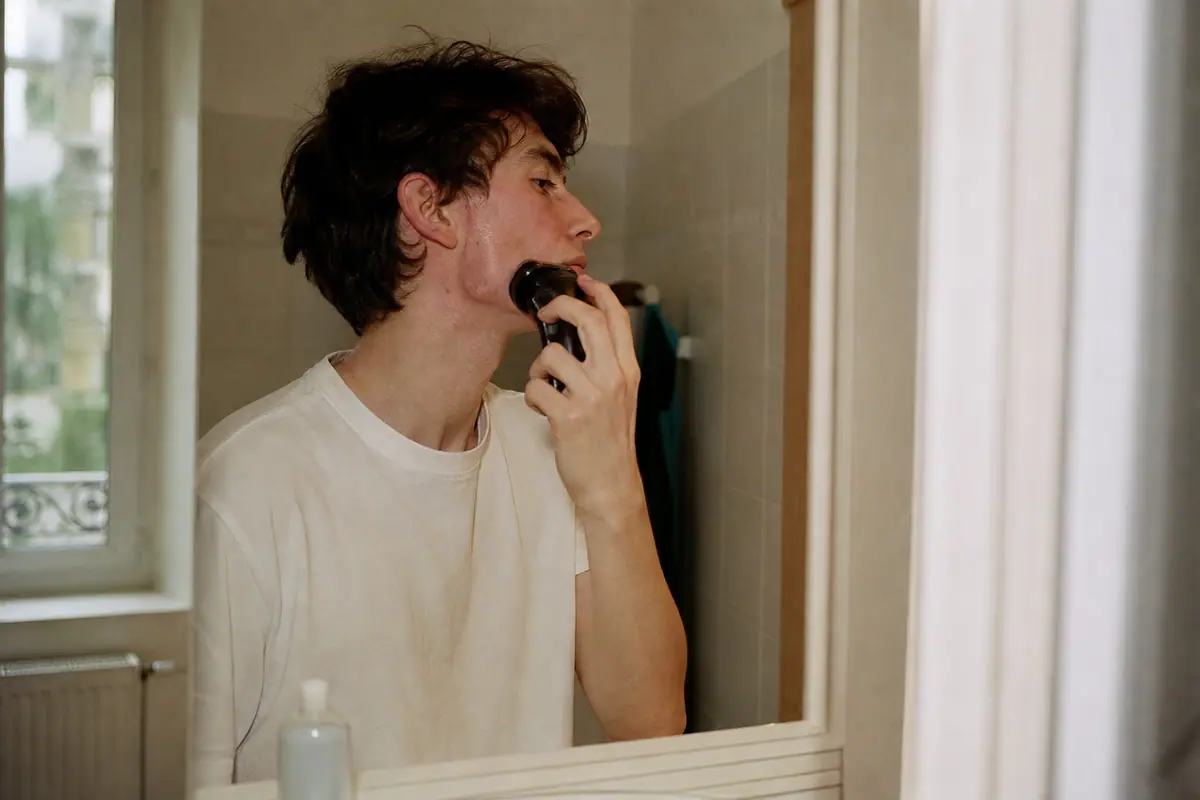 Un jeune homme à la peau sensible se rase délicatement le visage avec un rasoir électrique