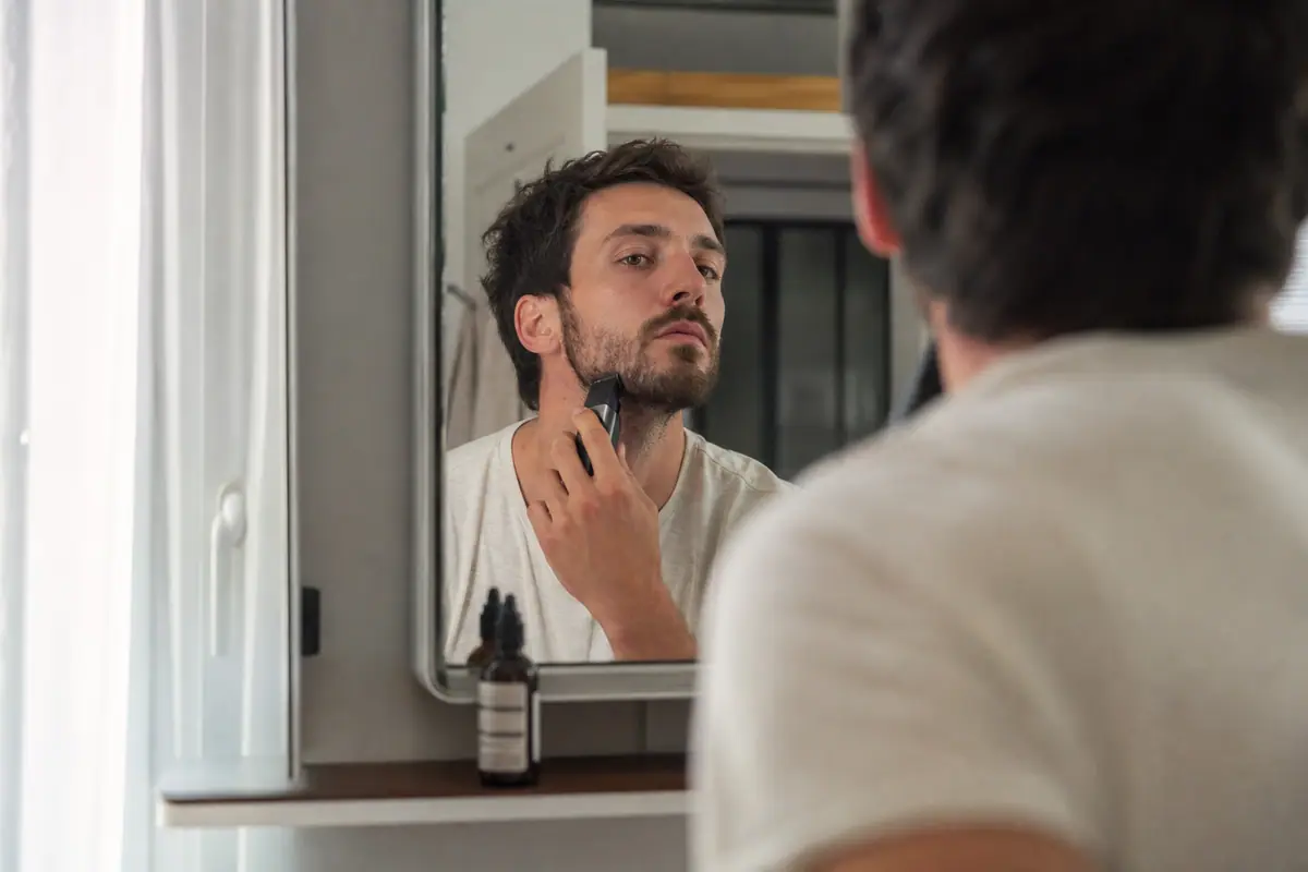 Un homme à la peau réactive entretient sa barbe avec précaution devant son miroir