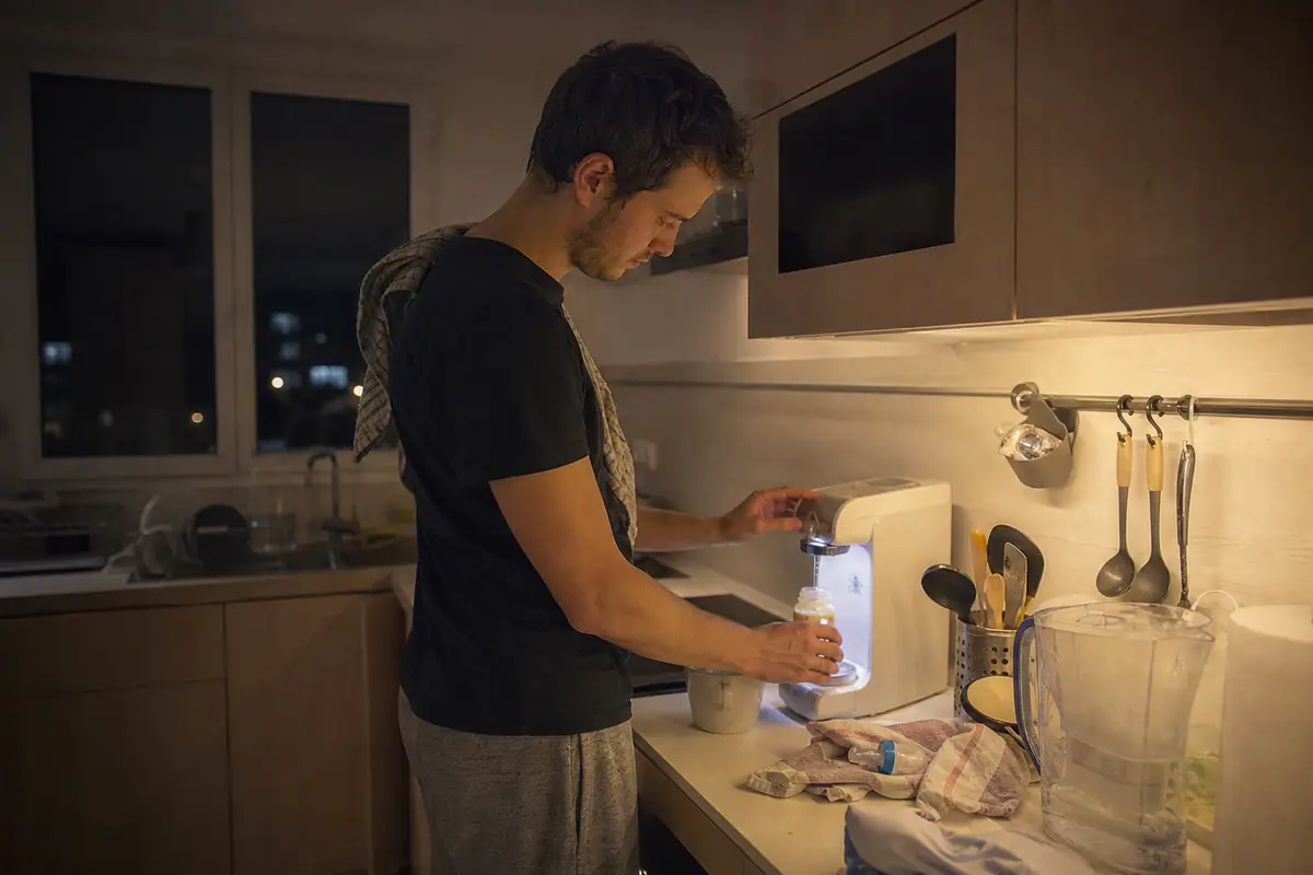 Un père prépare un biberon la nuit à l'aide d'une machine de préparation automatique dans sa cuisine