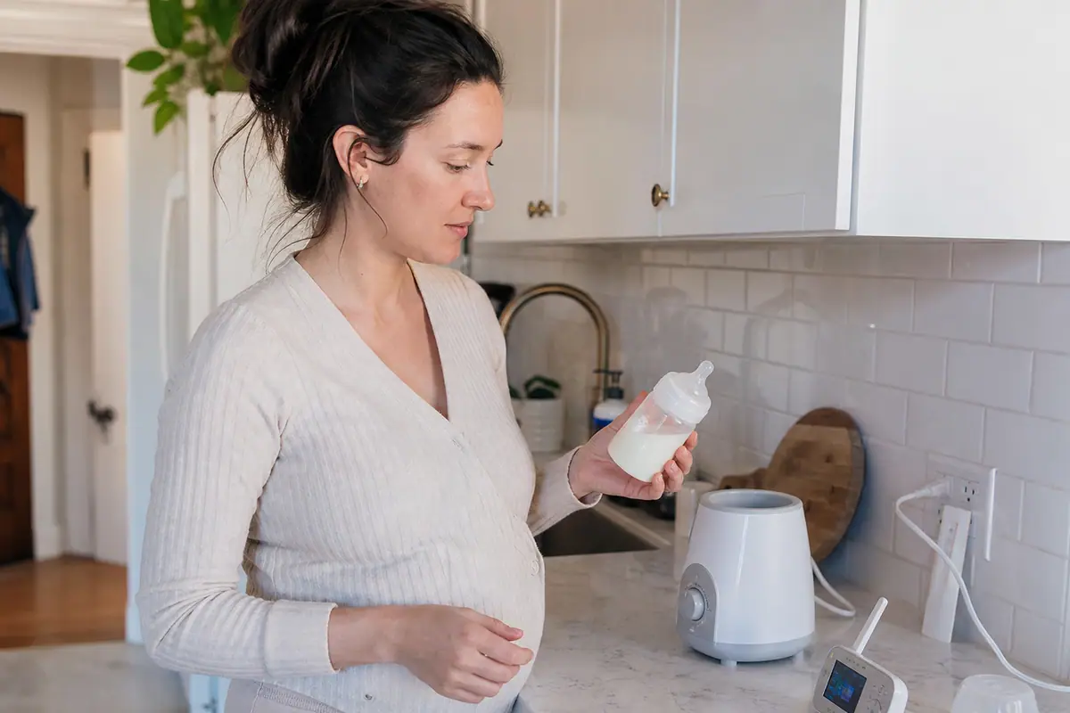 Une mère tient un biberon de lait maternel à côté d'un chauffe-biberon numérique dans sa cuisine