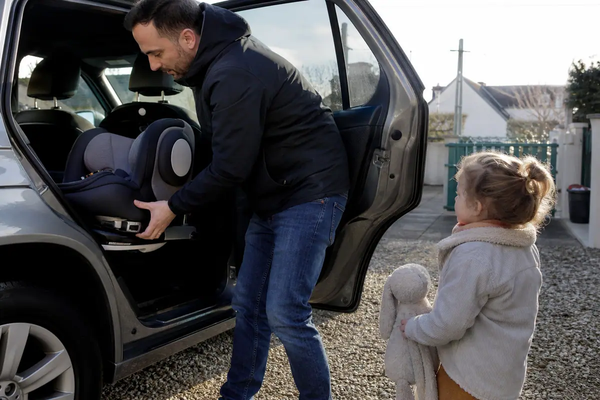 Un père fait pivoter un siège auto installé dos à la route pour y installer sa fille