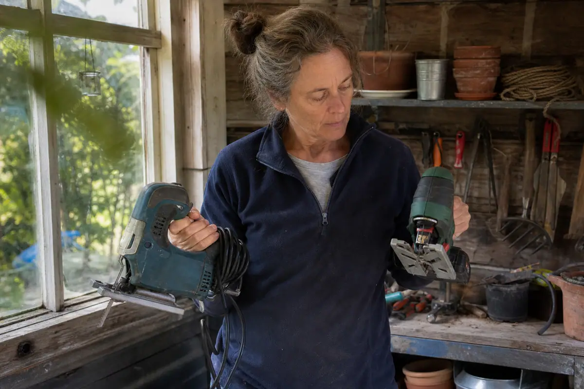 Une femme compare une scie sauteuse filaire et une scie sauteuse sans fil dans son abri de jardin