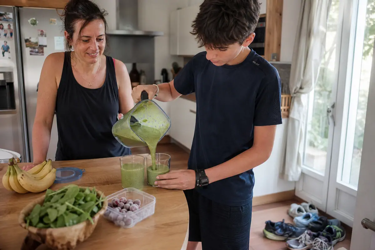 Un adolescent verse un smoothie vert du bol d'un blender pour lui et sa mère après un footing