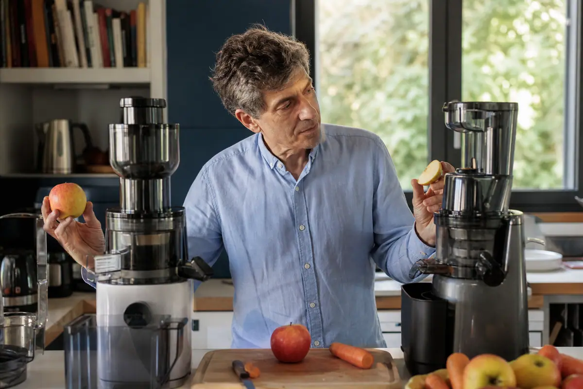 Un homme compare le goulot de deux extracteurs de jus verticaux avant de choisir
