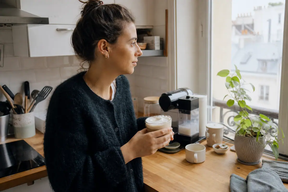 Une jeune femme tient un cappuccino préparé avec une machine à café à capsules équipée d'un réservoir à lait