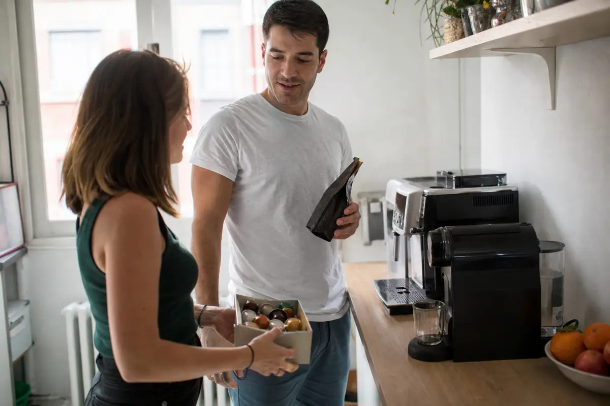 Un couple compare un sachet de café en grain et une boîte de capsules dans sa cuisine
