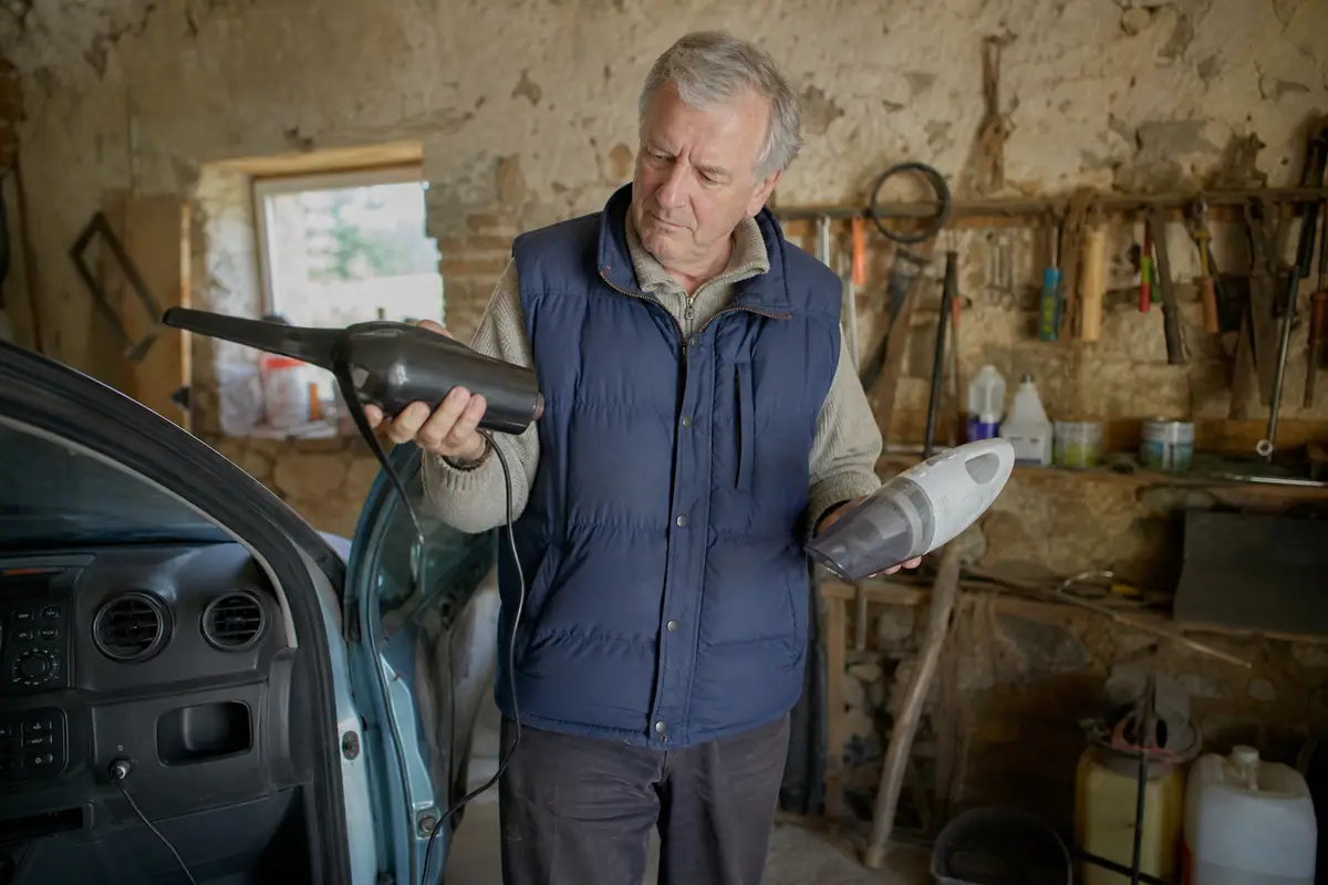 Un homme compare un aspirateur à main filaire branché sur la prise de sa voiture et un modèle sans fil