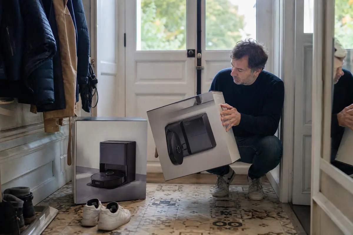 Un homme compare une simple base de charge et une station complète d'aspirateur robot dans l'entrée de son logement