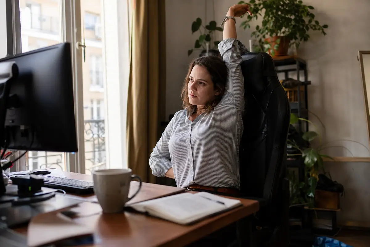 Une femme s'étire dans sa chaise gaming installée à son bureau, dans son appartement
