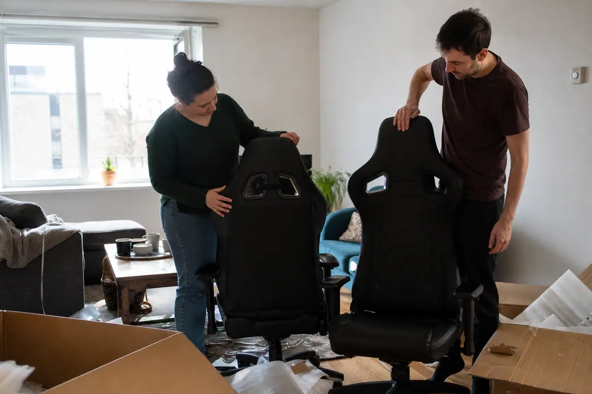Deux adultes comparent deux chaises gaming noires posées côte à côte dans un salon