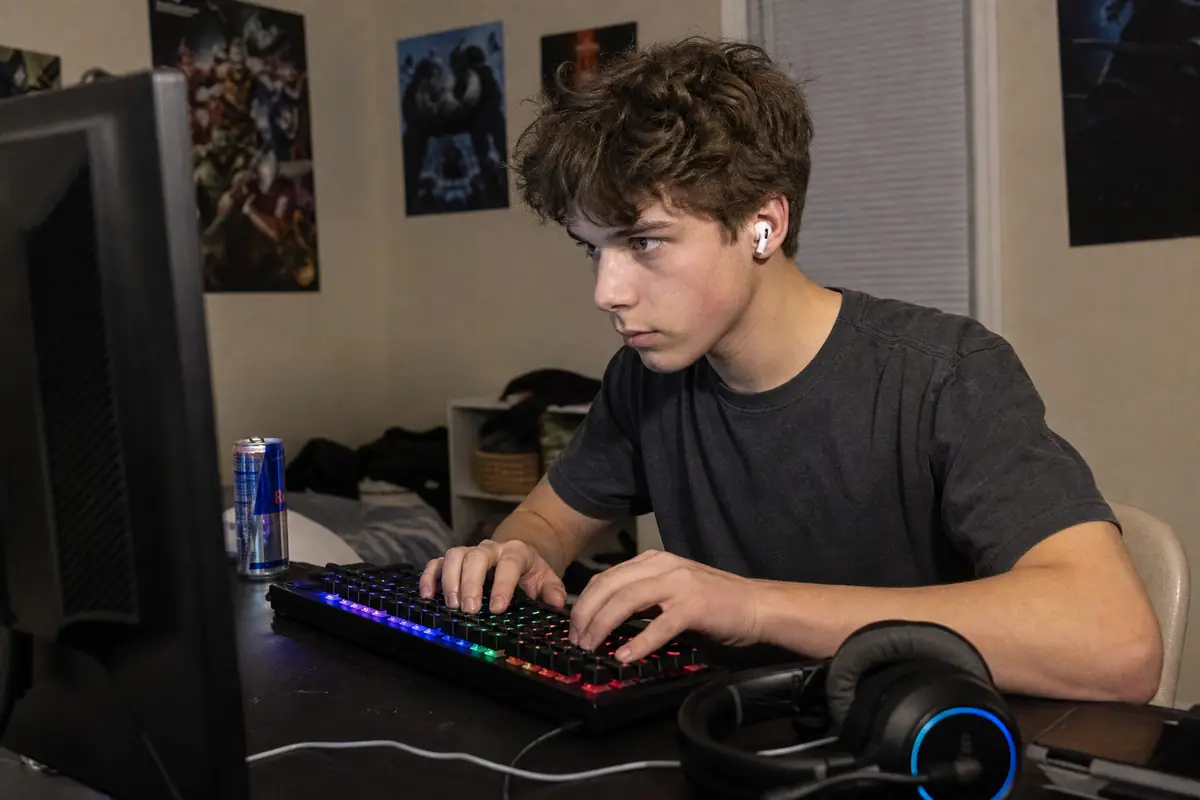 Un adolescent tape rapidement sur un clavier gaming mécanique rétroéclairé, le soir dans sa chambre