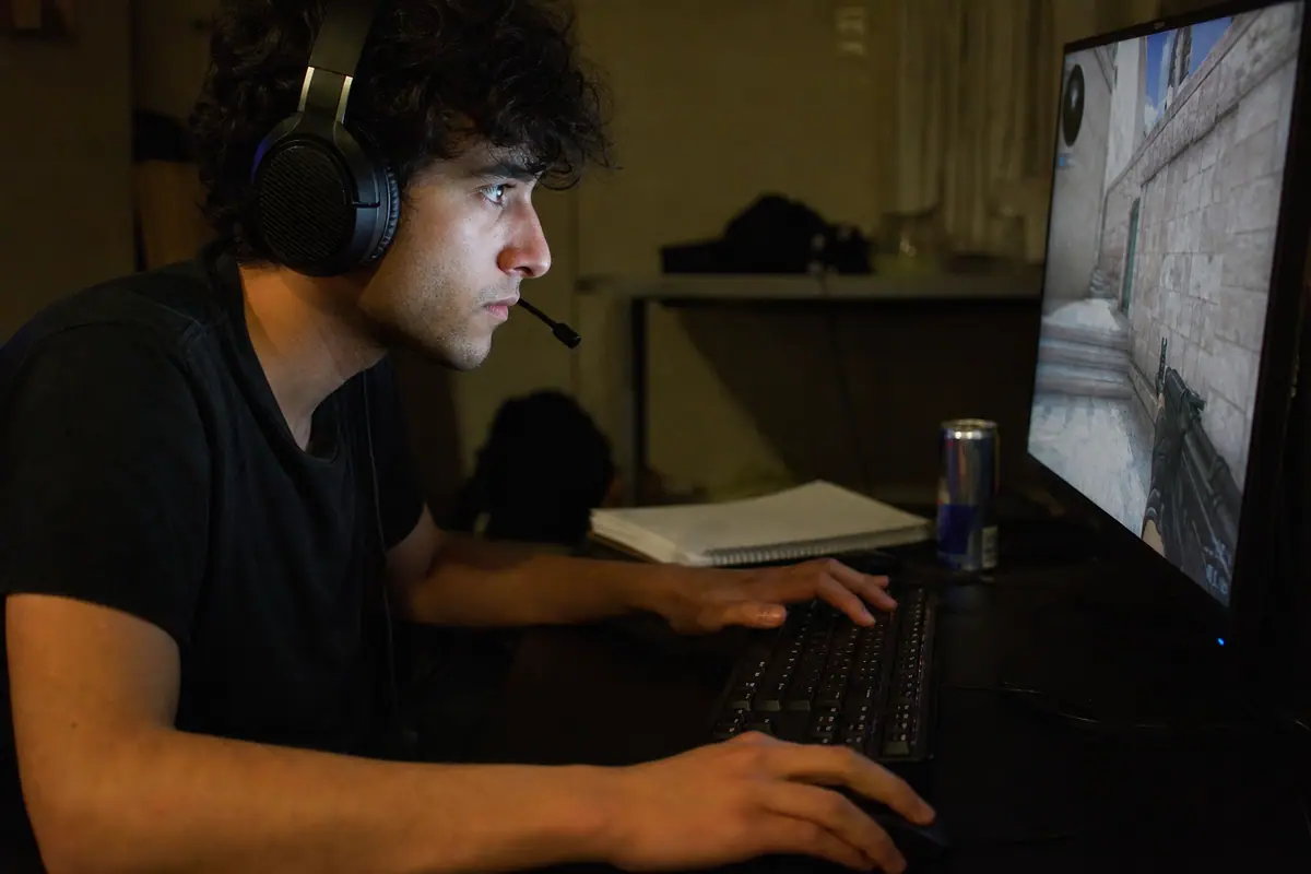 Un jeune homme concentré joue à un jeu de tir compétitif, les mains rapides sur un clavier gaming mécanique