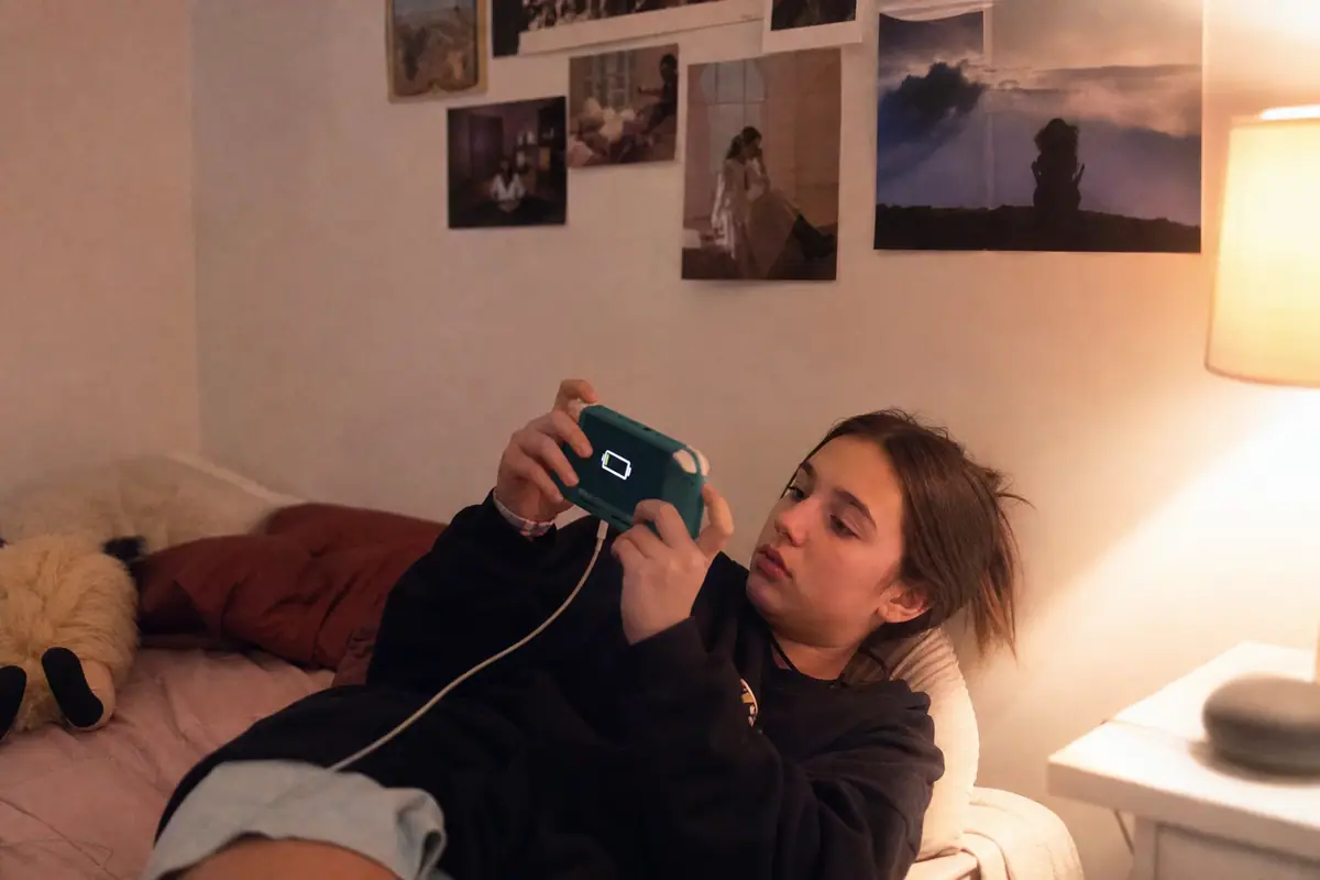 Une adolescente vérifie le niveau de batterie de sa console portable en charge dans sa chambre, le soir