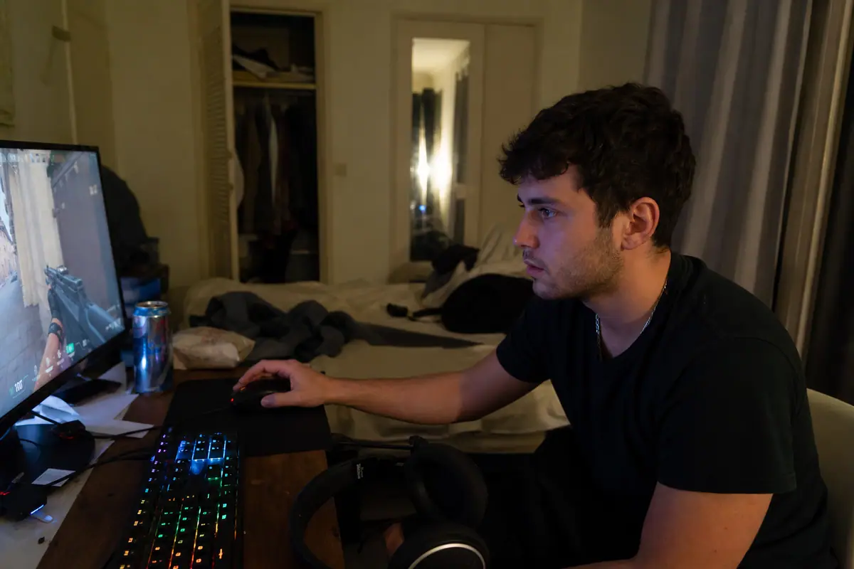 Un jeune homme concentré tient une souris gaming sans fil devant son écran en pleine partie de jeu de tir