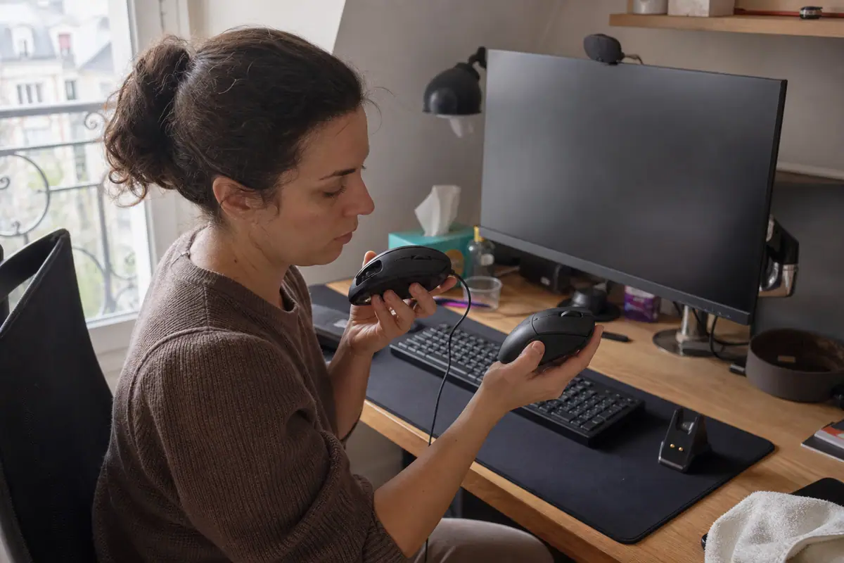 Une femme compare une souris gaming filaire encore branchée avec une souris sans fil en charge sur son bureau