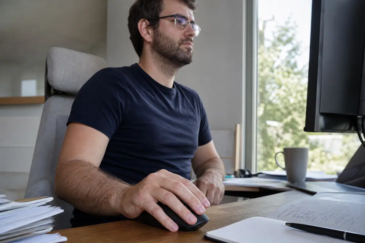 Un homme aux grandes mains teste la prise en main d'une souris gaming ergonomique à son bureau