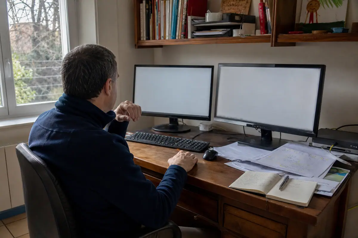 Un homme compare deux écrans PC posés côte à côte sur son bureau à la maison