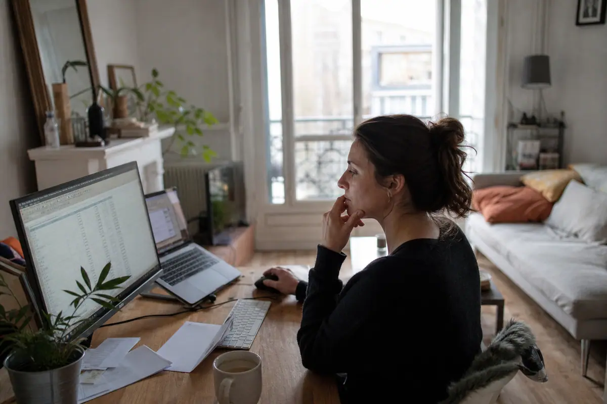 Une femme en télétravail travaille devant un grand écran PC posé sur un bureau en bois