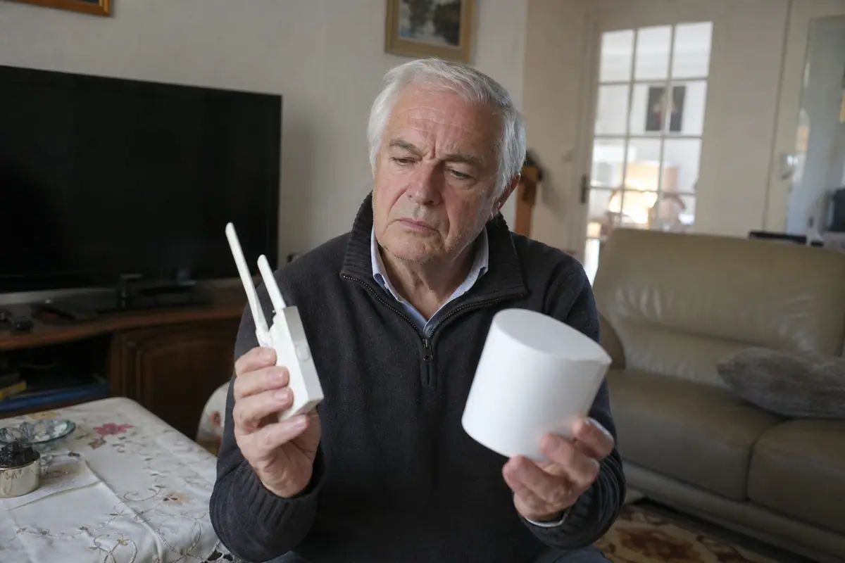 Un homme compare un ancien répéteur Wifi et une borne de système mesh dans son salon
