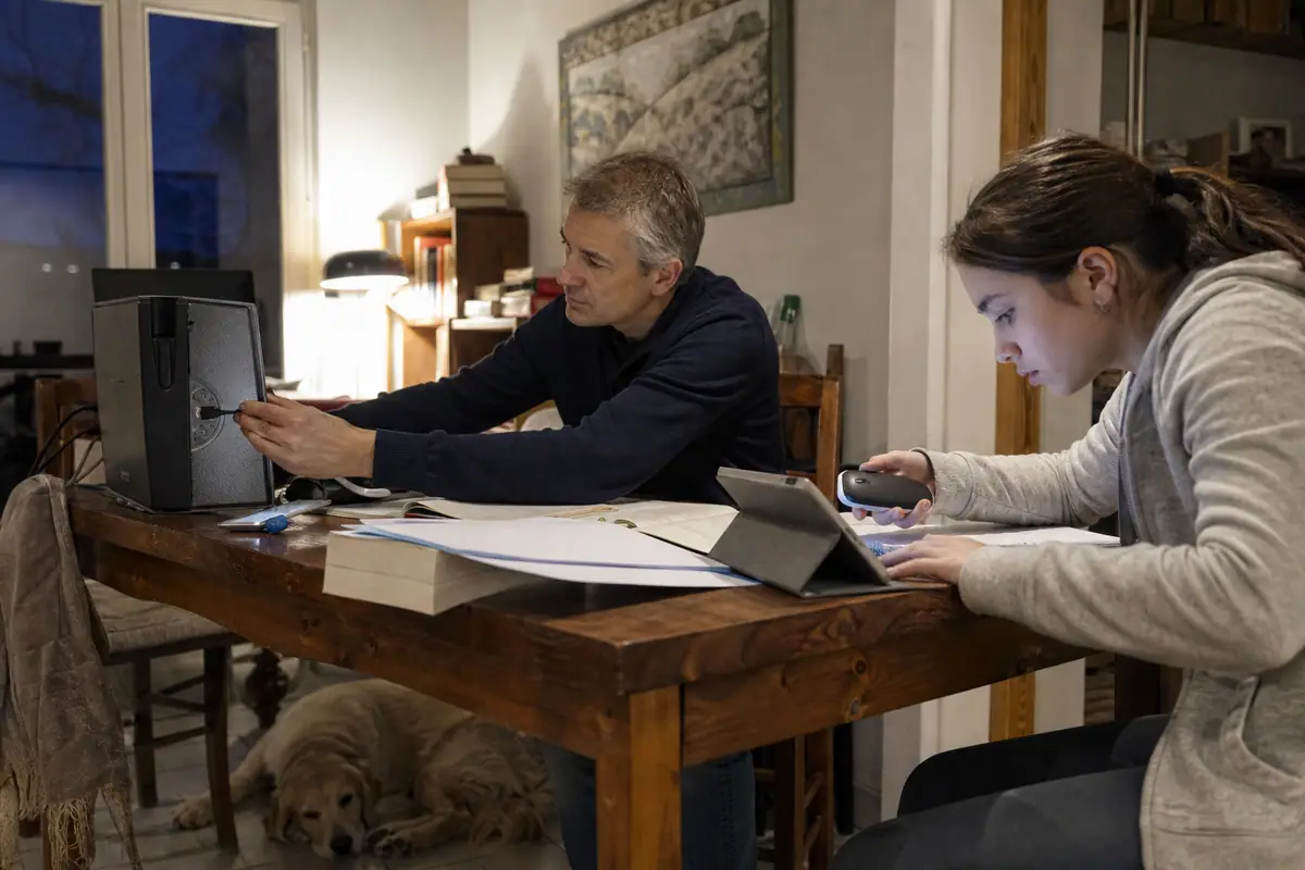 Un père branche un petit récepteur USB sur un ordinateur pendant que sa fille jumelle une souris avec sa tablette