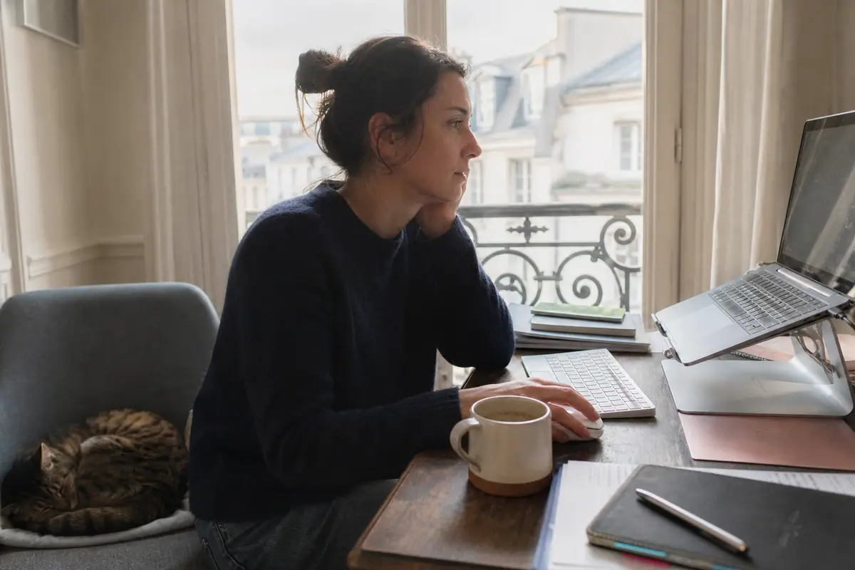 Une femme en télétravail utilise une souris sans fil ergonomique à côté de son ordinateur portable surélevé