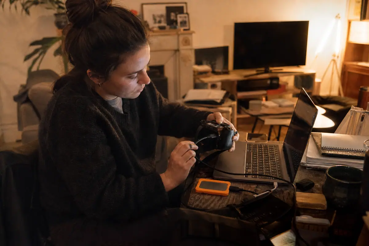 Une monteuse vidéo transfère des rushs vers un petit SSD externe branché à son ordinateur portable dans son salon