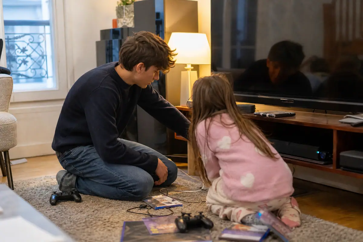 Un adolescent et sa petite sœur branchent un SSD externe sur leur console de jeu dans le salon