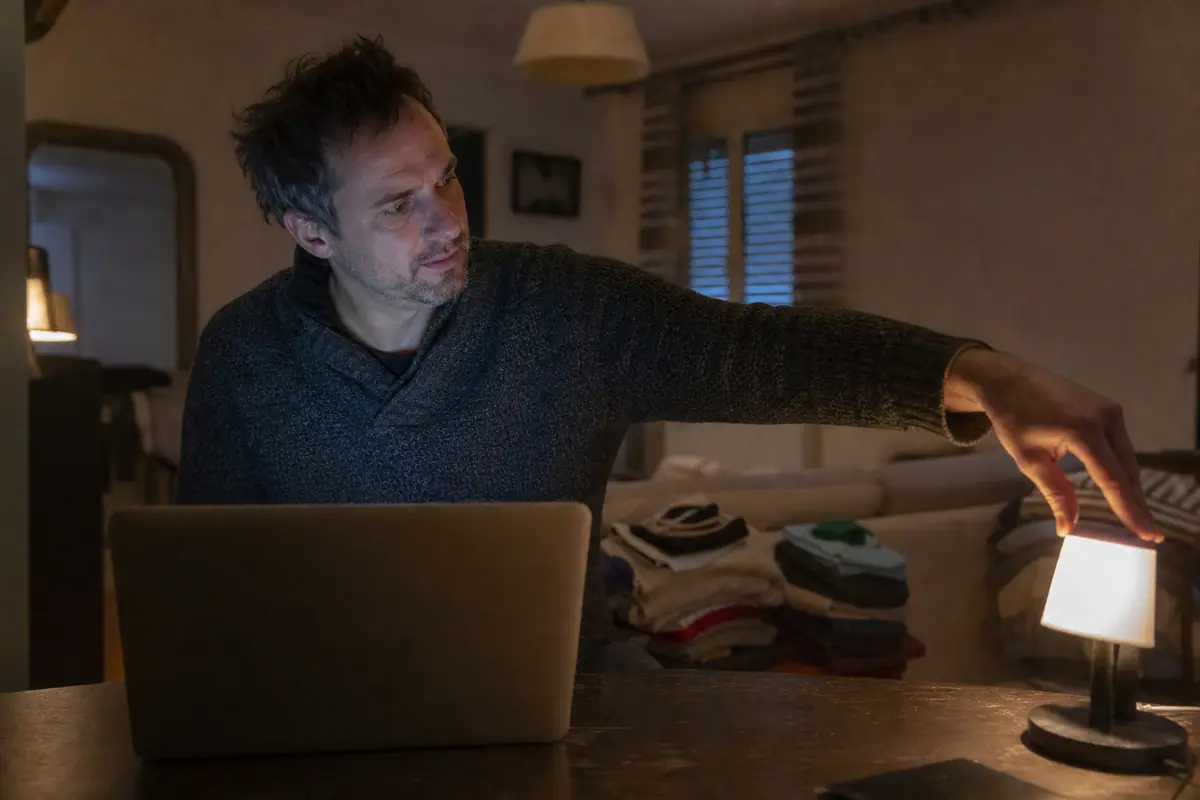 Un homme installe une petite lampe derrière son ordinateur pour éclairer son visage avant une visioconférence