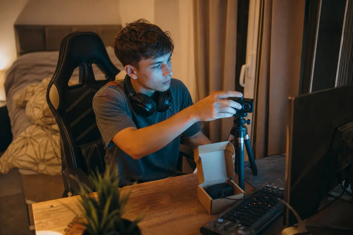 Un jeune homme règle une webcam posée sur un mini trépied à côté de son écran dans sa chambre