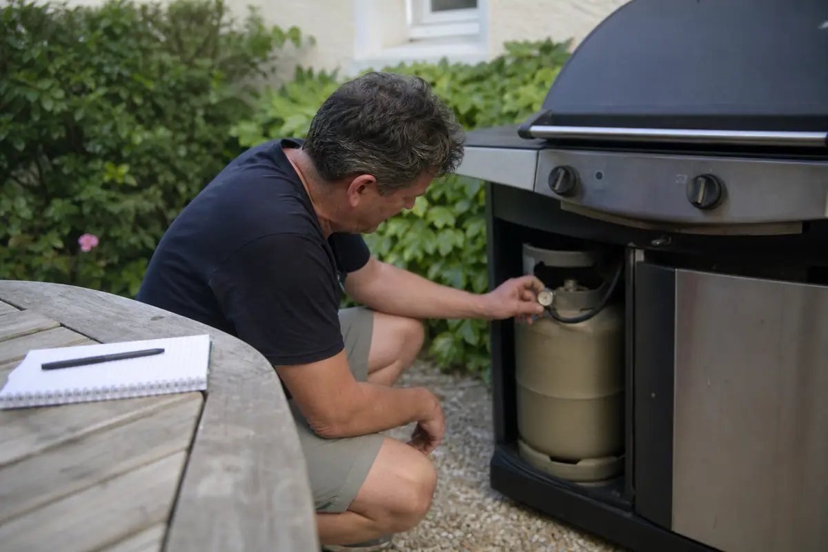 Un homme vérifie le niveau d'une bouteille de gaz reliée à son barbecue avant une session de grillades