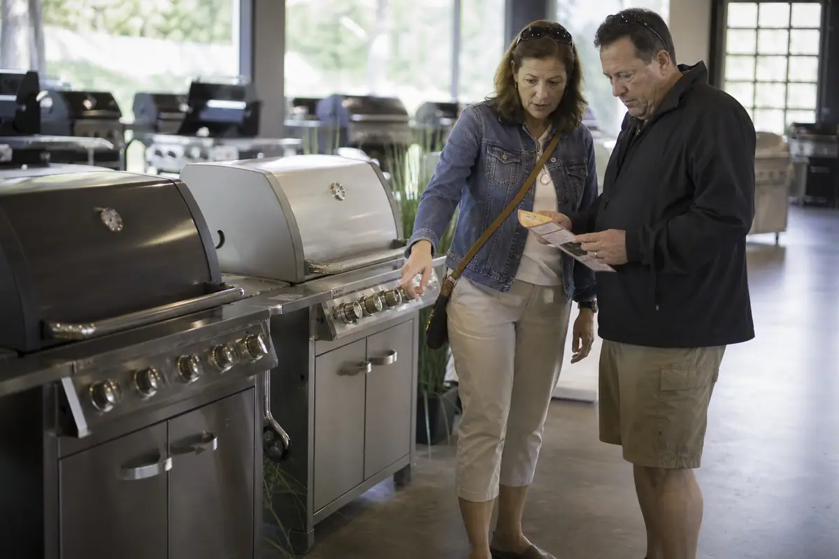 Un couple compare deux barbecues à gaz côte à côte dans un magasin de jardin