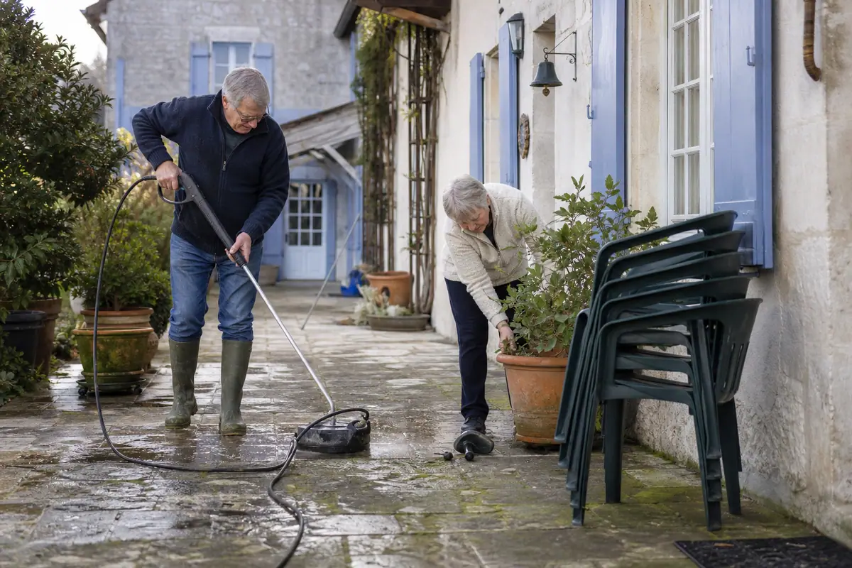 Un couple de retraités nettoie une terrasse en pierre couverte de mousse avec un laveur de surface haute pression