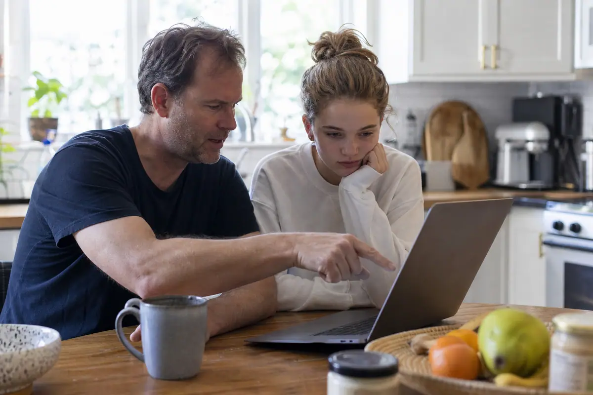 Un père et sa fille comparent ensemble deux options d'abonnement pour une caméra de surveillance sur un ordinateur portable