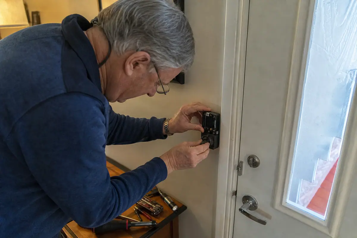 Un homme change les piles d'une serrure connectée fixée à l'intérieur de sa porte d'entrée