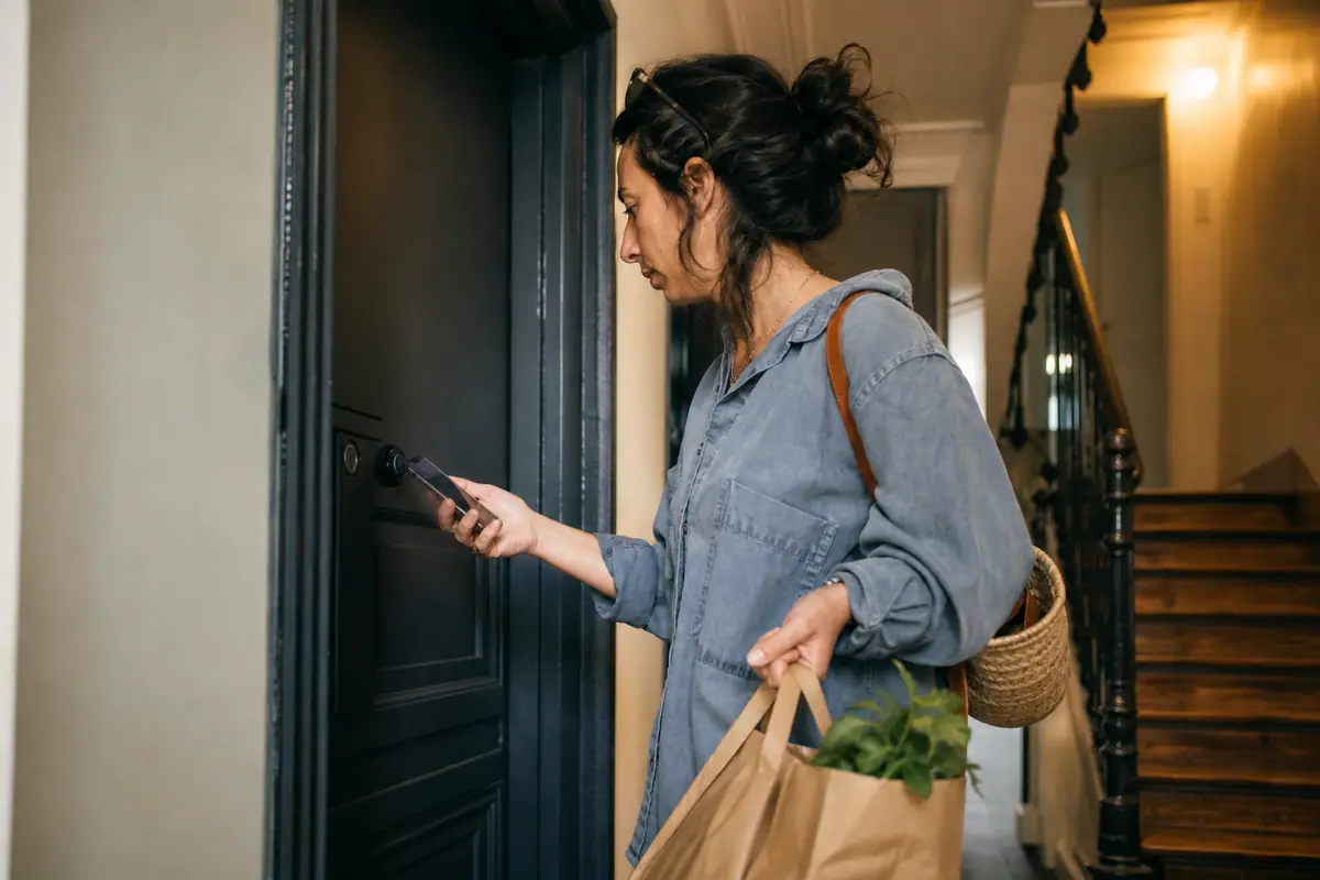 Une femme déverrouille la porte de son appartement avec son smartphone grâce à une serrure connectée