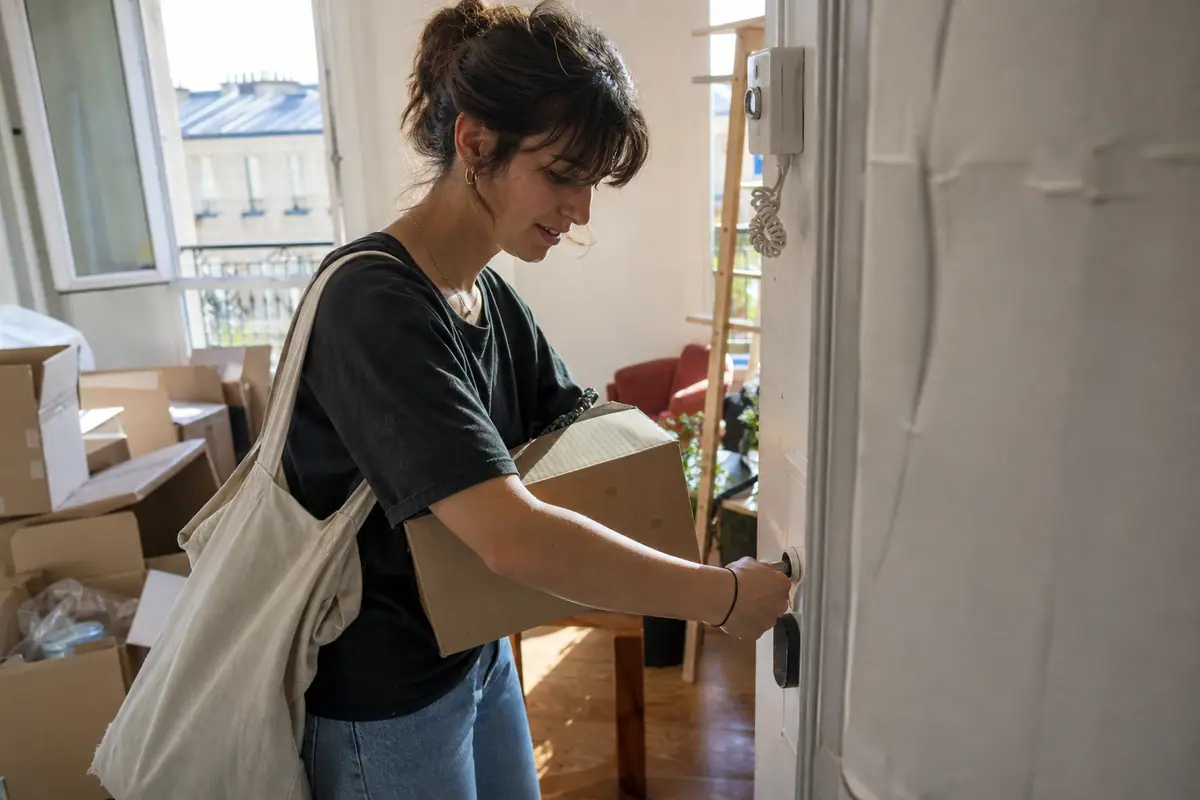 Une jeune locataire installe une serrure connectée sur la porte de son nouvel appartement le jour de son emménagement