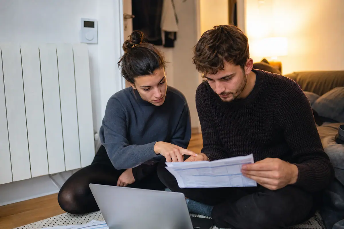 Un couple compare sa facture d'énergie et les données de son thermostat connecté sur un ordinateur portable